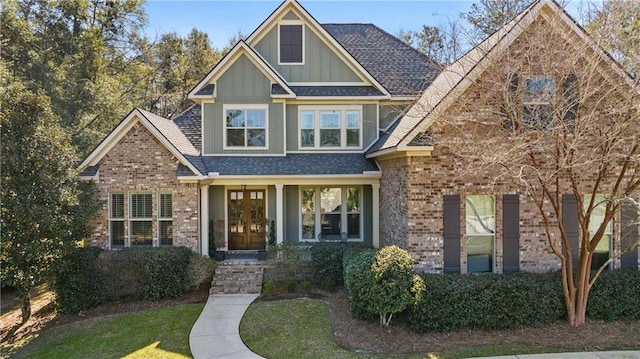 craftsman inspired home with roof with shingles, a front lawn, board and batten siding, and brick siding