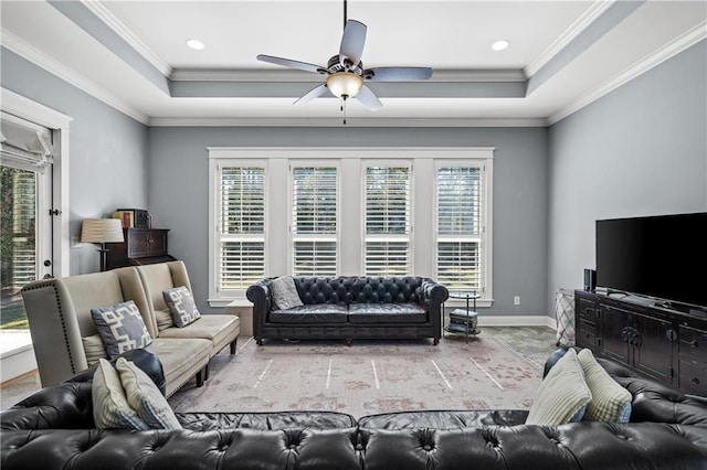 living area with a ceiling fan, a tray ceiling, crown molding, and baseboards