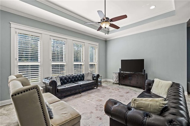 living room featuring baseboards, ornamental molding, a raised ceiling, and a ceiling fan