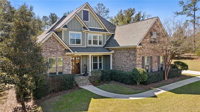 craftsman-style home featuring roof with shingles, a front lawn, board and batten siding, and brick siding