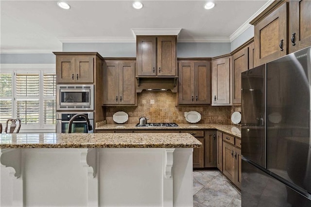 kitchen with light stone counters, backsplash, appliances with stainless steel finishes, ornamental molding, and under cabinet range hood