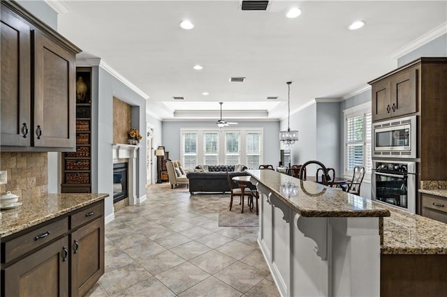 kitchen featuring appliances with stainless steel finishes, a glass covered fireplace, ornamental molding, light stone countertops, and a kitchen bar