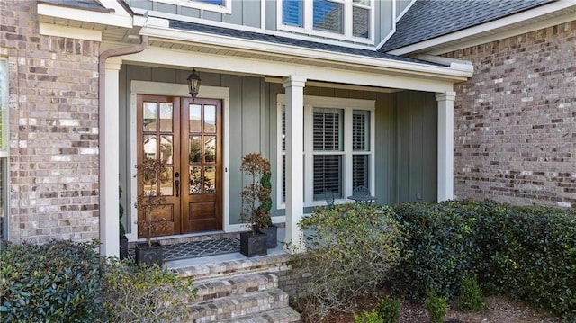 doorway to property featuring a shingled roof, french doors, brick siding, and board and batten siding