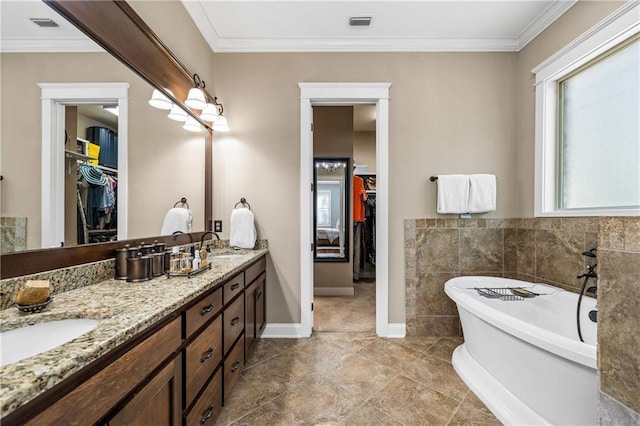 bathroom with double vanity, ornamental molding, a spacious closet, a freestanding bath, and a sink