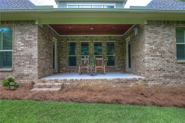 property entrance with a patio area, a shingled roof, and brick siding