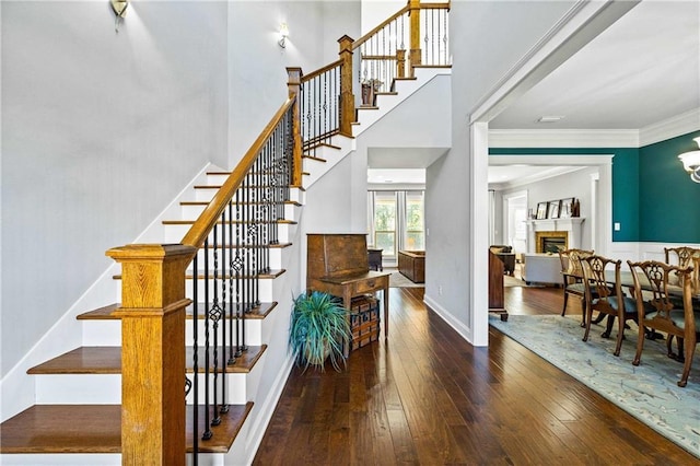 stairs with baseboards, ornamental molding, wood finished floors, a high ceiling, and a fireplace