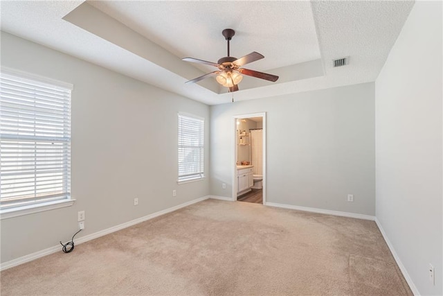 empty room with ceiling fan, plenty of natural light, light colored carpet, and a raised ceiling