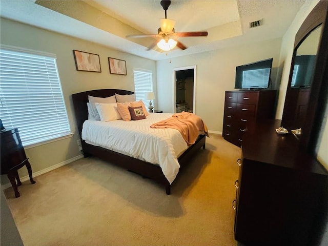 bedroom with ceiling fan, light colored carpet, a spacious closet, and a raised ceiling