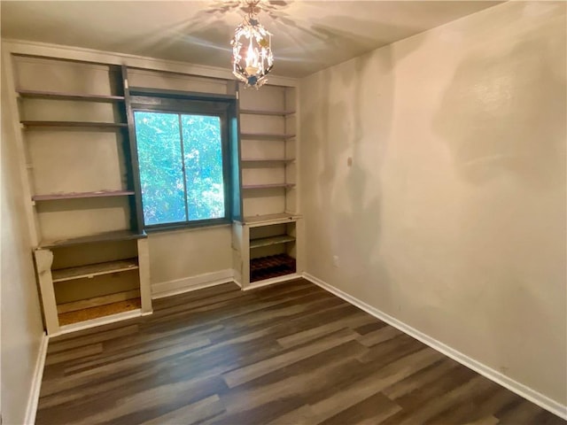 spare room featuring dark wood-type flooring and a notable chandelier