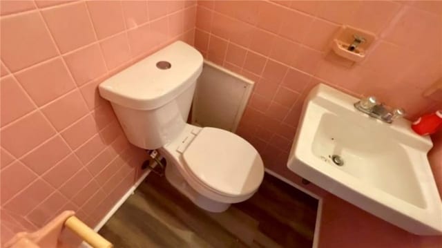 bathroom featuring toilet, sink, wood-type flooring, and tile walls