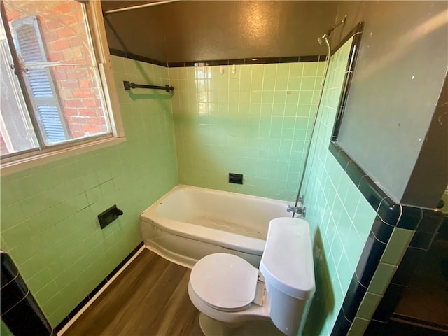 bathroom featuring tile walls, hardwood / wood-style floors, tiled shower / bath combo, and toilet