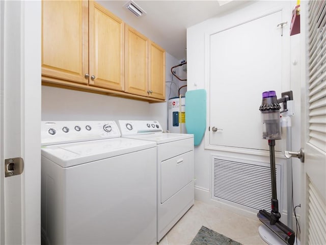 washroom featuring light tile patterned floors, water heater, washing machine and clothes dryer, and cabinets