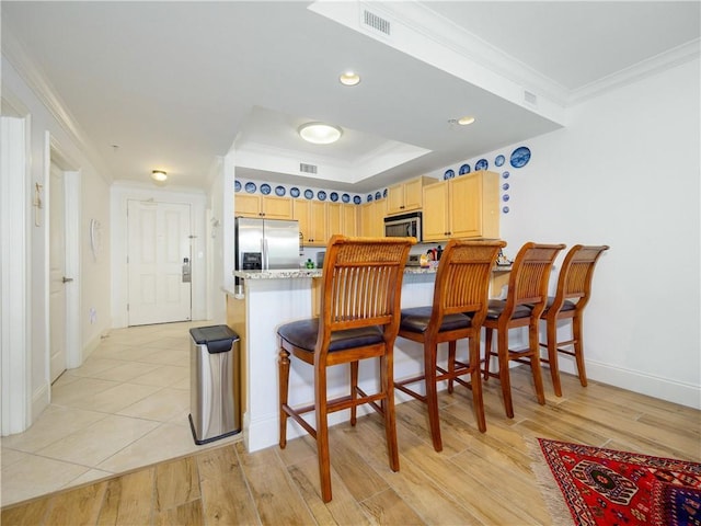 kitchen featuring stainless steel refrigerator with ice dispenser, a breakfast bar, light brown cabinets, and ornamental molding