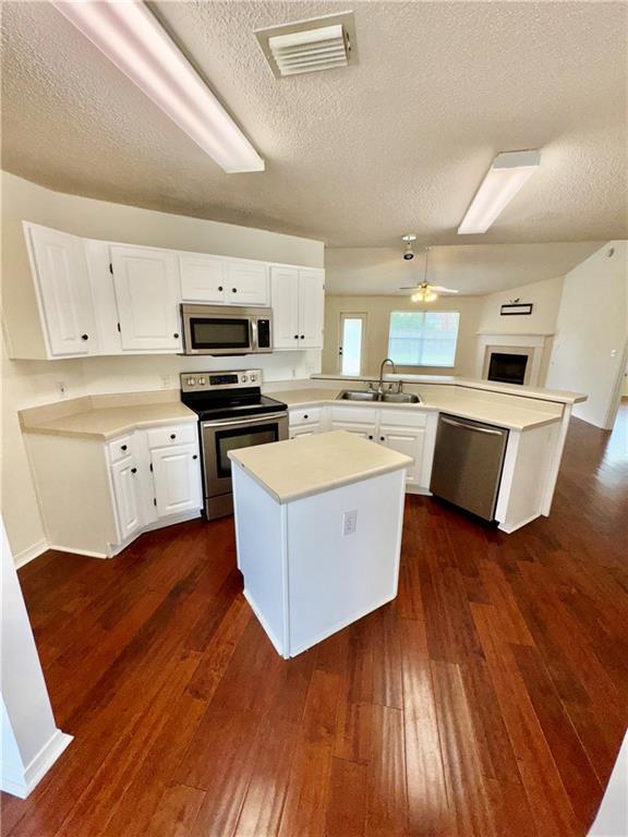 kitchen featuring sink, dark wood-type flooring, appliances with stainless steel finishes, white cabinetry, and kitchen peninsula