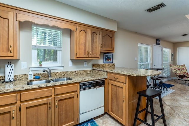 kitchen with visible vents, a breakfast bar, a peninsula, white dishwasher, and a sink