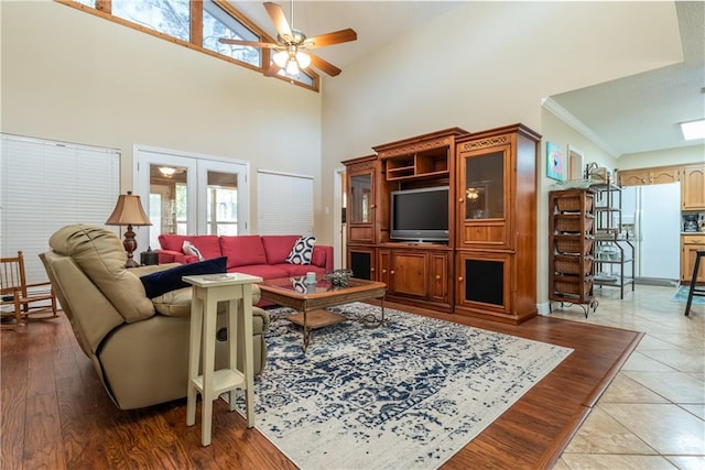 living area with ceiling fan, a high ceiling, crown molding, french doors, and light wood-style floors