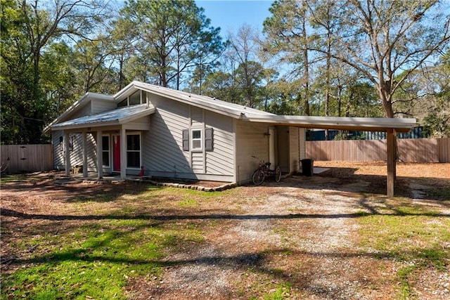 view of front of home with dirt driveway, a carport, and fence