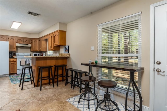 kitchen with white appliances, visible vents, a peninsula, under cabinet range hood, and a kitchen bar