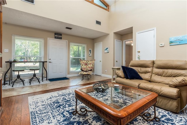 living area featuring a high ceiling, visible vents, light wood finished floors, and baseboards