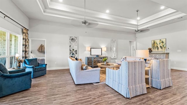 living room with hardwood / wood-style flooring, a high ceiling, ceiling fan, a raised ceiling, and ornamental molding