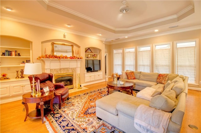 living room with crown molding, a raised ceiling, a high end fireplace, ceiling fan, and light hardwood / wood-style flooring