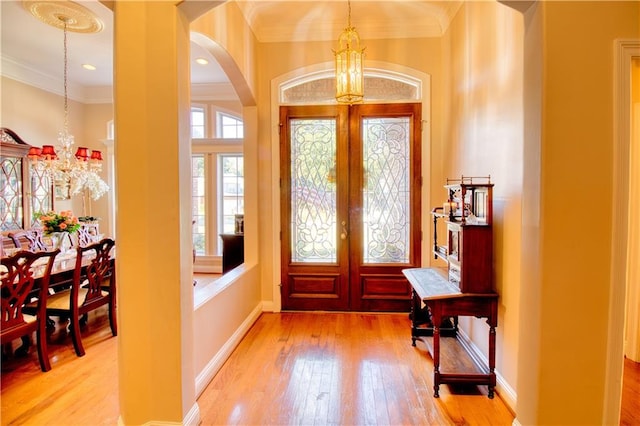 entryway featuring an inviting chandelier, crown molding, light hardwood / wood-style flooring, and french doors