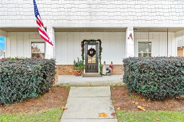 doorway to property with covered porch, brick siding, and board and batten siding