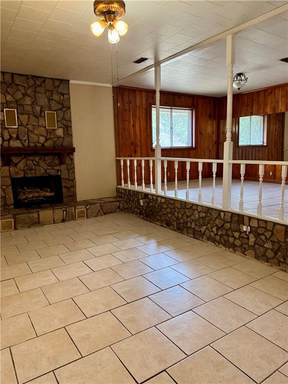 interior space featuring wooden walls, a stone fireplace, light tile patterned floors, and a wealth of natural light