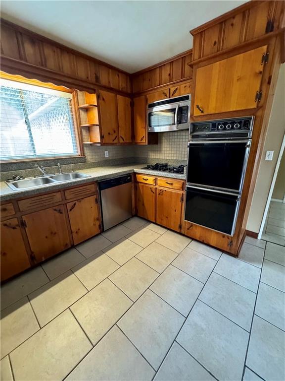 kitchen featuring tasteful backsplash, light tile patterned floors, sink, and black appliances