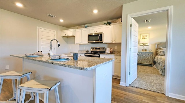 kitchen with white cabinetry, light hardwood / wood-style floors, appliances with stainless steel finishes, a kitchen breakfast bar, and light stone countertops