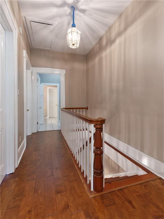 hallway featuring attic access, wood-type flooring, baseboards, and an upstairs landing