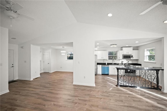 kitchen with appliances with stainless steel finishes, white cabinetry, wood-type flooring, lofted ceiling, and ceiling fan