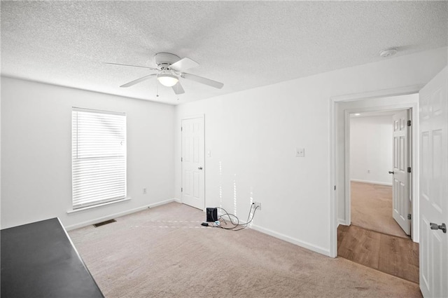 empty room with ceiling fan, light carpet, and a textured ceiling