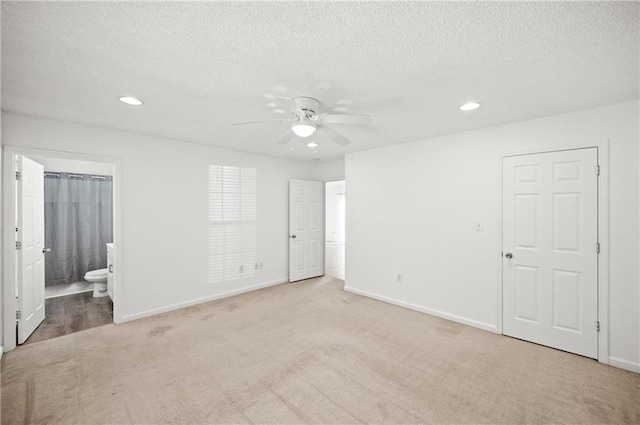 unfurnished bedroom with ceiling fan, light colored carpet, ensuite bath, and a textured ceiling