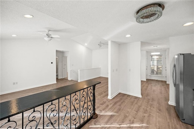 hallway featuring vaulted ceiling, a textured ceiling, and light hardwood / wood-style floors