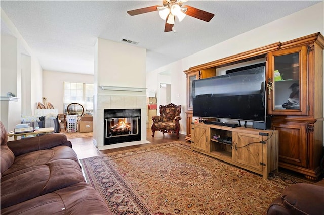 living room with a tile fireplace, a textured ceiling, light hardwood / wood-style flooring, and ceiling fan