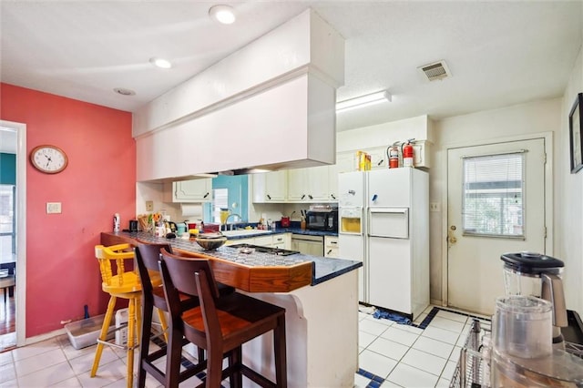 kitchen featuring a breakfast bar, white refrigerator with ice dispenser, kitchen peninsula, and light tile patterned floors