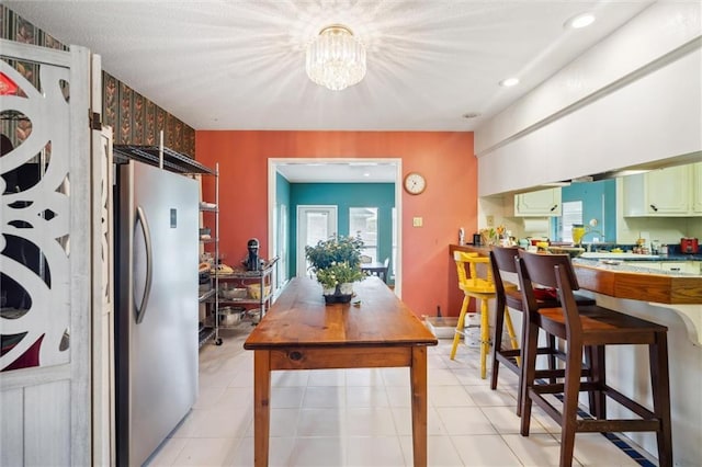 kitchen with an inviting chandelier, light tile patterned floors, stainless steel fridge, and green cabinets