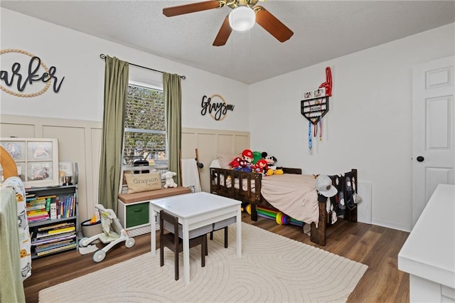 bedroom with a decorative wall, wood finished floors, wainscoting, and a textured ceiling