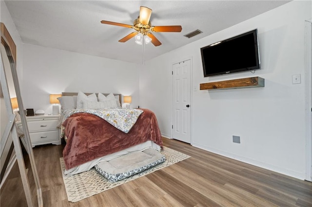 bedroom with ceiling fan, wood finished floors, visible vents, and baseboards