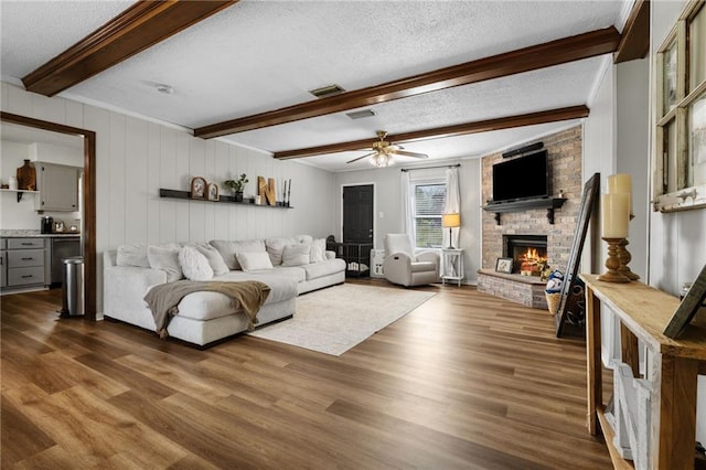 living area featuring visible vents, beam ceiling, a textured ceiling, dark wood finished floors, and a brick fireplace