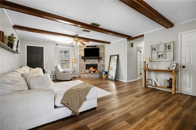 living room featuring beam ceiling, a stone fireplace, wood finished floors, a textured ceiling, and a ceiling fan