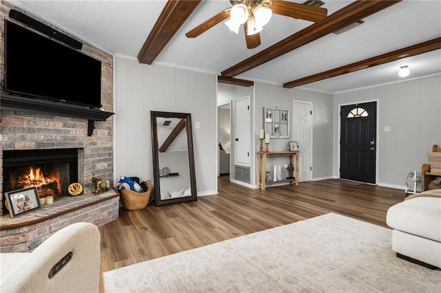 living area featuring a ceiling fan, a brick fireplace, beamed ceiling, and wood finished floors