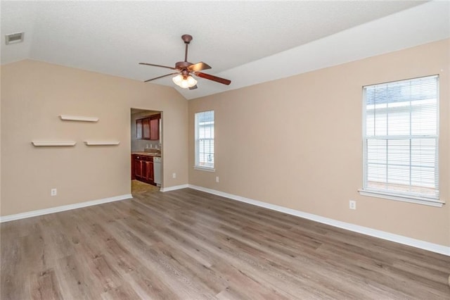 empty room featuring ceiling fan, plenty of natural light, light hardwood / wood-style floors, and vaulted ceiling