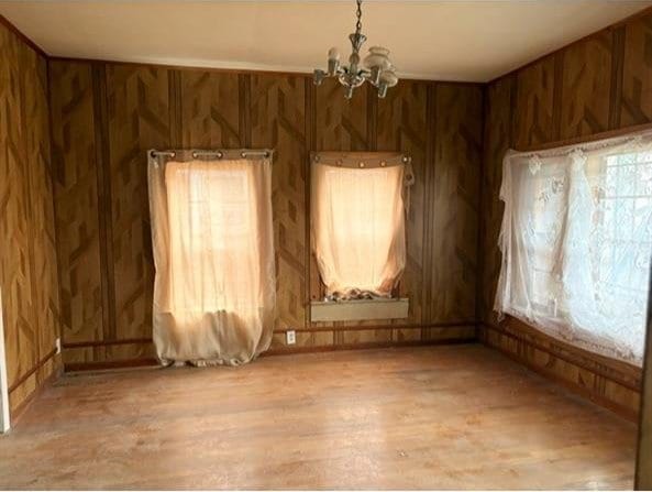 empty room with wood walls, light wood-type flooring, and an inviting chandelier