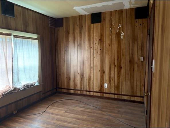 unfurnished room with wooden walls and dark wood-type flooring