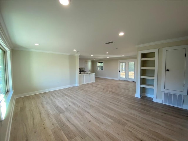 unfurnished living room with built in shelves, crown molding, and light hardwood / wood-style floors