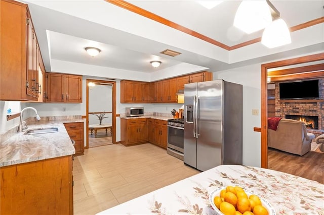 kitchen with a brick fireplace, a raised ceiling, sink, light stone countertops, and appliances with stainless steel finishes