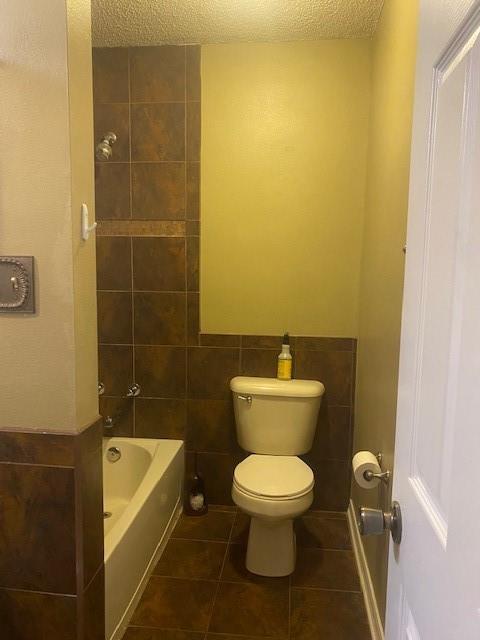 bathroom with tile walls, tiled shower / bath combo, a textured ceiling, tile patterned floors, and toilet