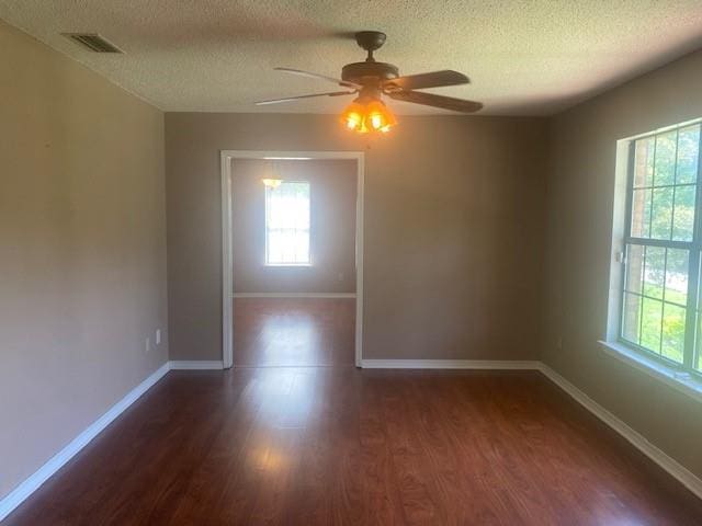 empty room with dark wood-type flooring, plenty of natural light, and a textured ceiling